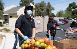 hispanic male pushing a cart of apples, potatoes, onion and avacados.